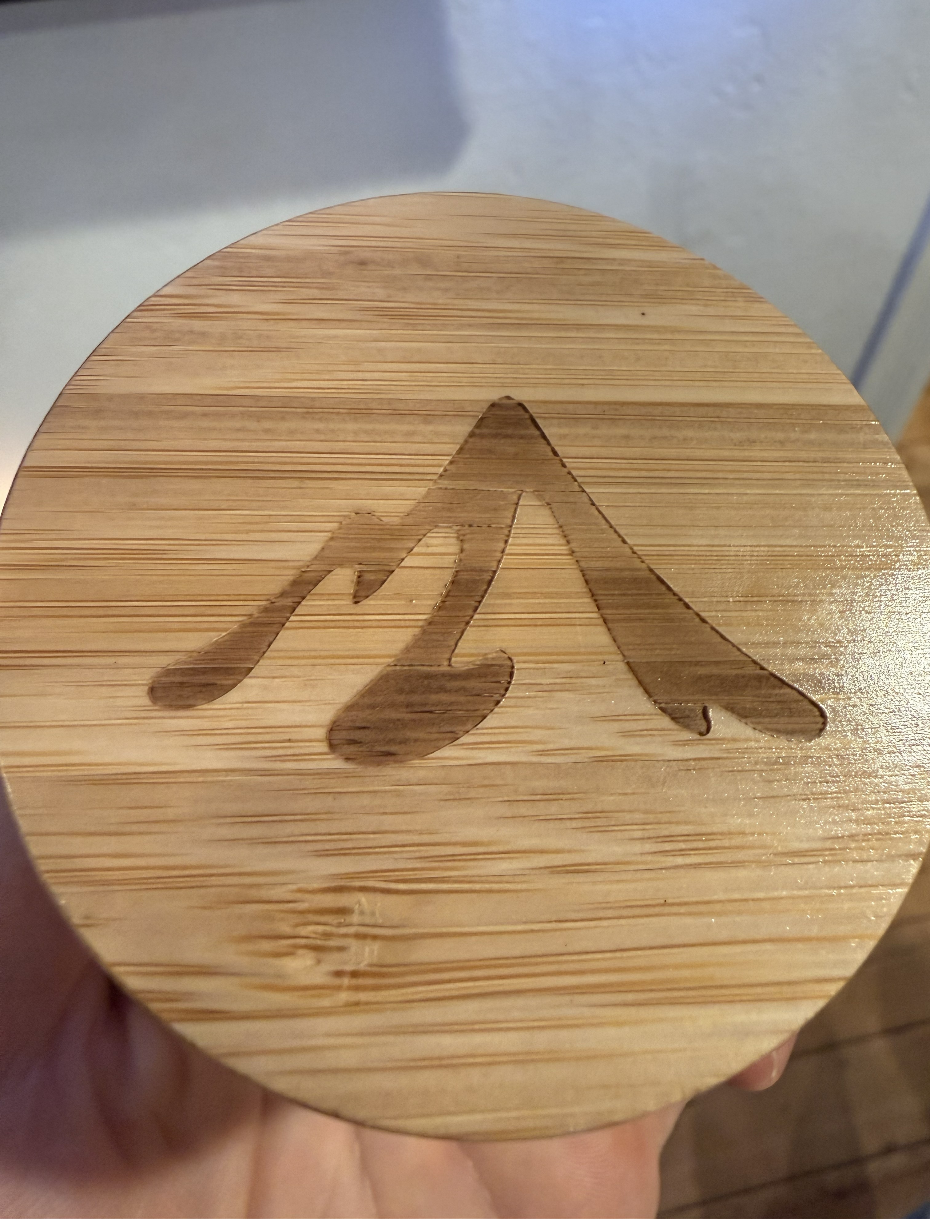 A close-up of a circular bamboo lid with a stylized mountain design etched into its surface.