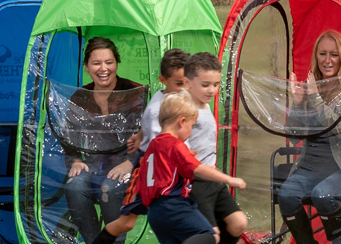 Two women in colorful personal pop-up tents watch three young boys play in front of them.