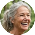 A circular headshot of a smiling older woman with long gray hair pulled back in a ponytail.