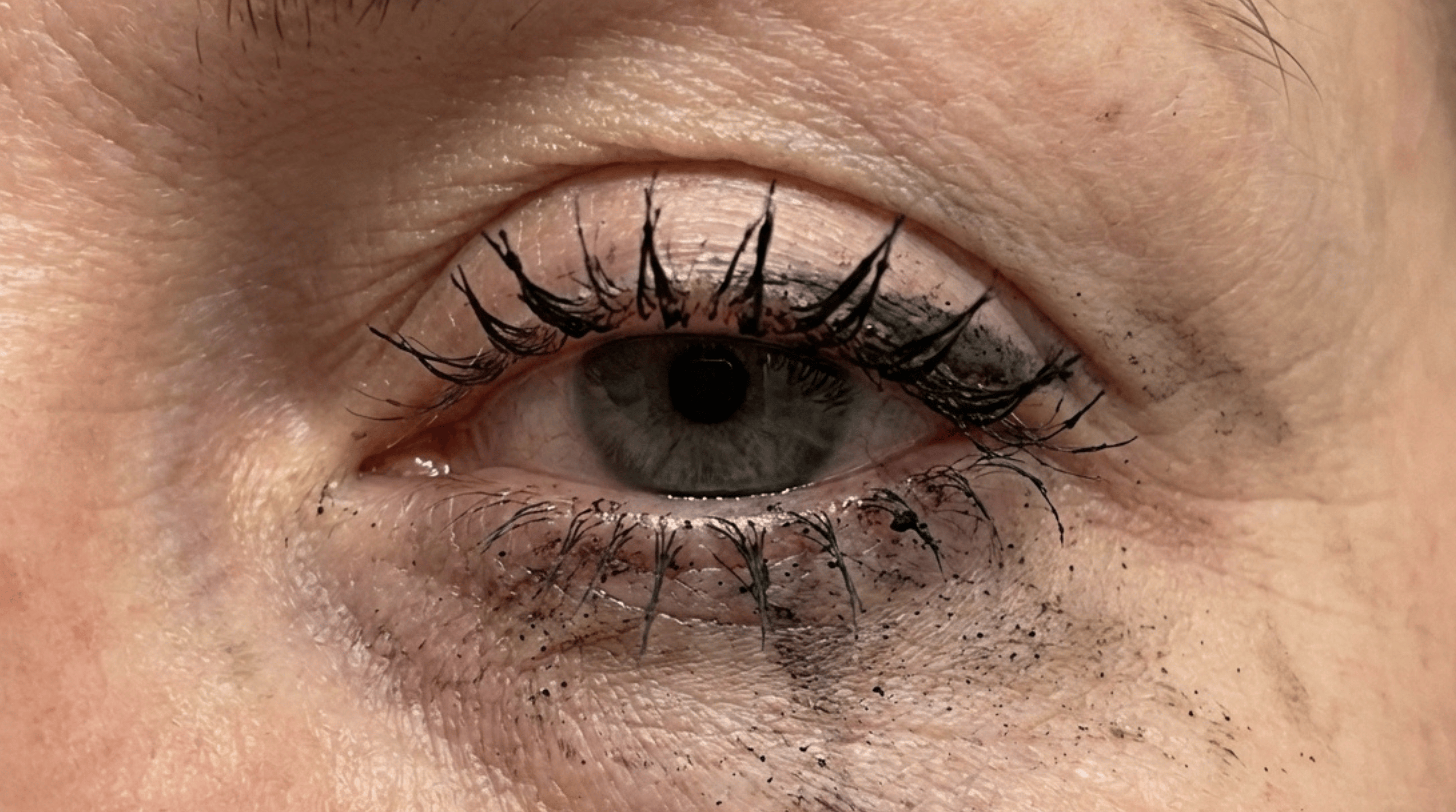 A close-up of an eye with smudged and running black mascara on the eyelid and under-eye area.