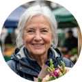 A smiling older woman with white hair, holding a bouquet of flowers outdoors.