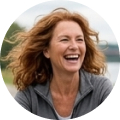 A middle-aged woman with wavy red hair laughing while looking to her right, wearing a grey jacket.