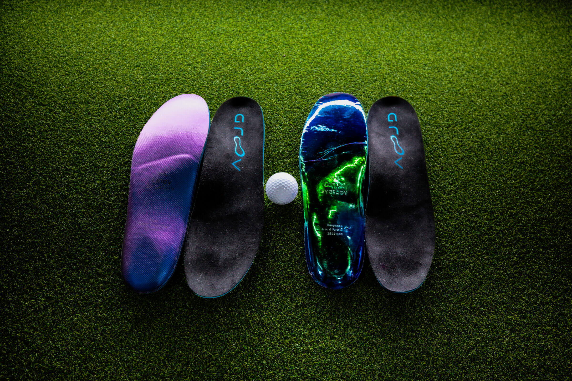 Four colorful insoles and a golf ball on green turf.