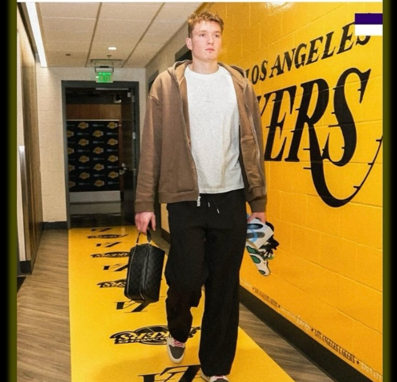 Person walking in a hallway with Los Angeles Lakers branding, carrying a bag.