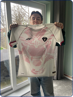 Person holding a white jersey with a red graphic design, standing indoors by a window.