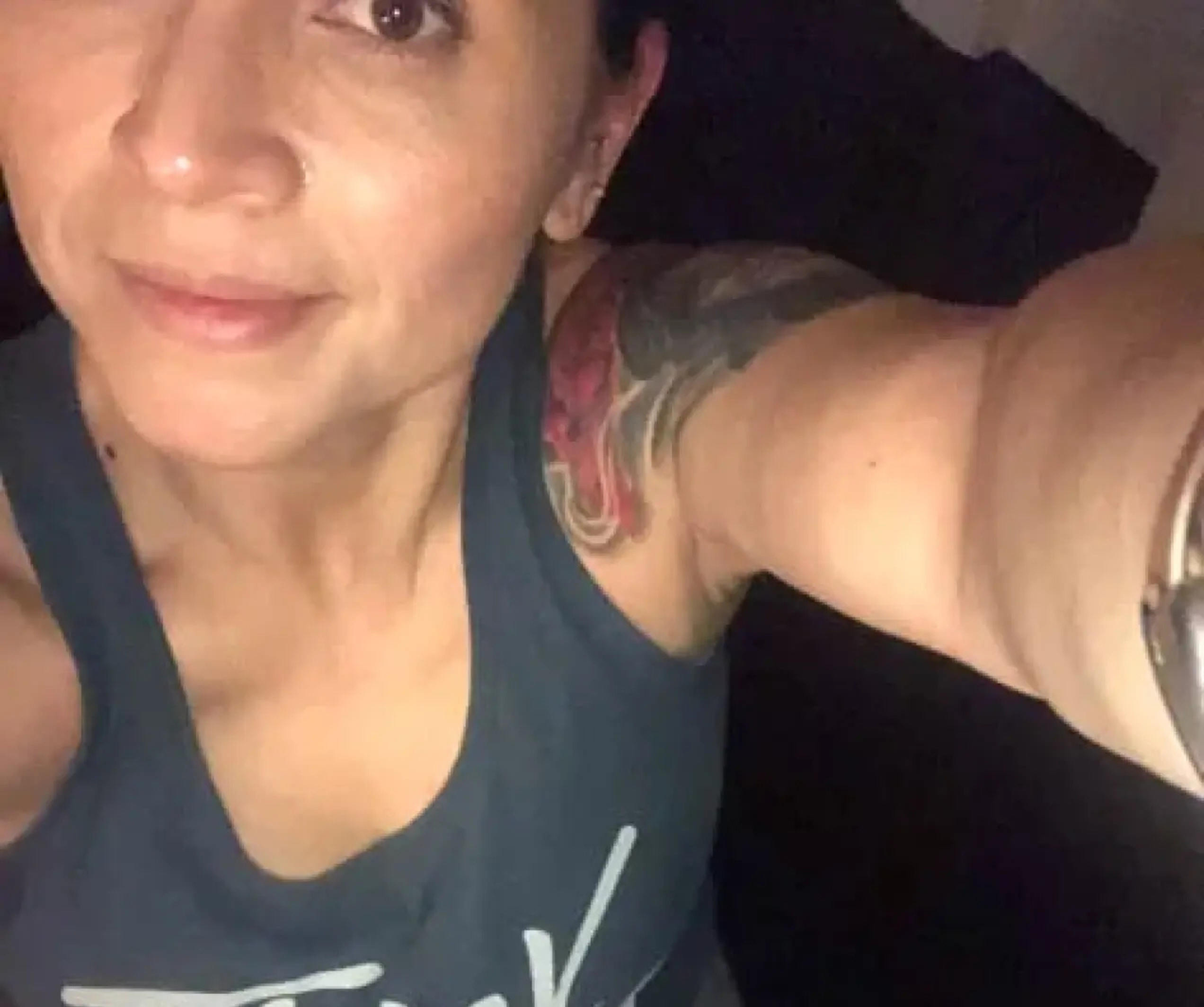 Person taking a selfie, showing a tattooed arm and wearing a blue tank top.