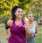 Two women jogging outdoors with earphones, smiling.