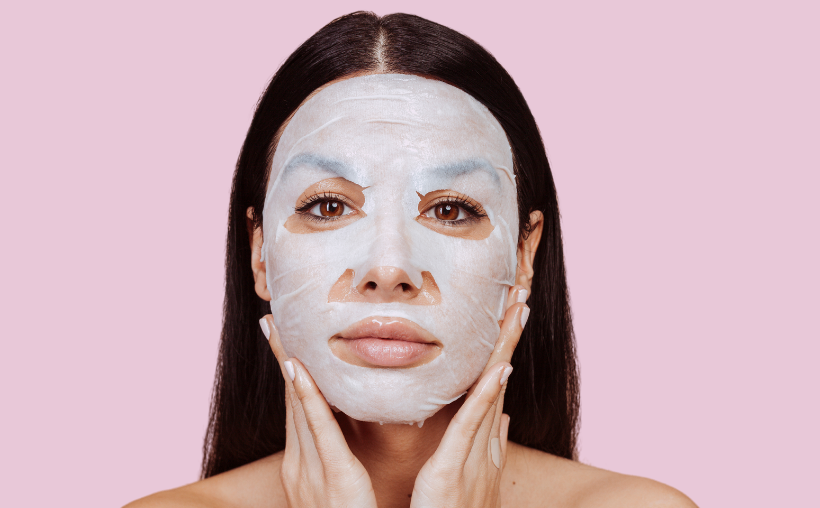 Person wearing a white sheet face mask against a pink background.