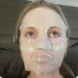 Person wearing a sheet mask on their face, lying on a dark surface.