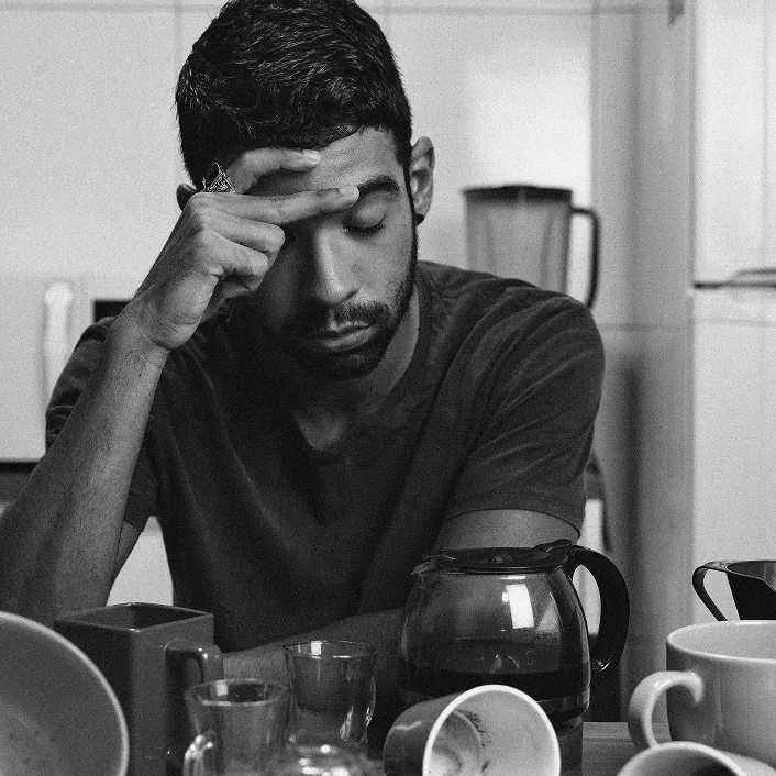 Person sitting with closed eyes, surrounded by coffee mugs and a pot.