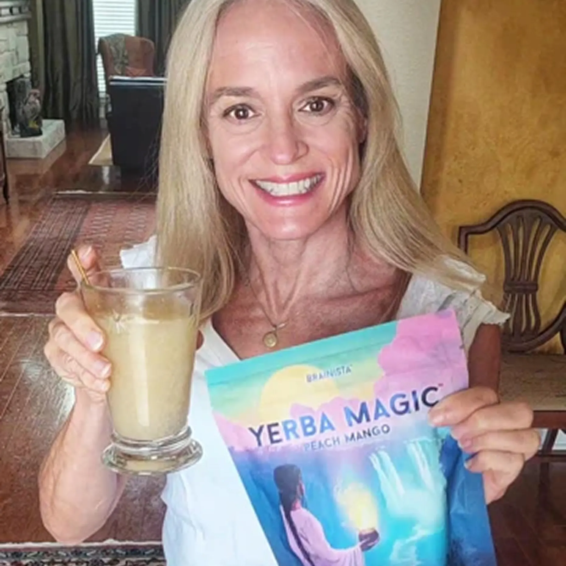 Person holding a glass and a Yerba Magic product package, smiling indoors.