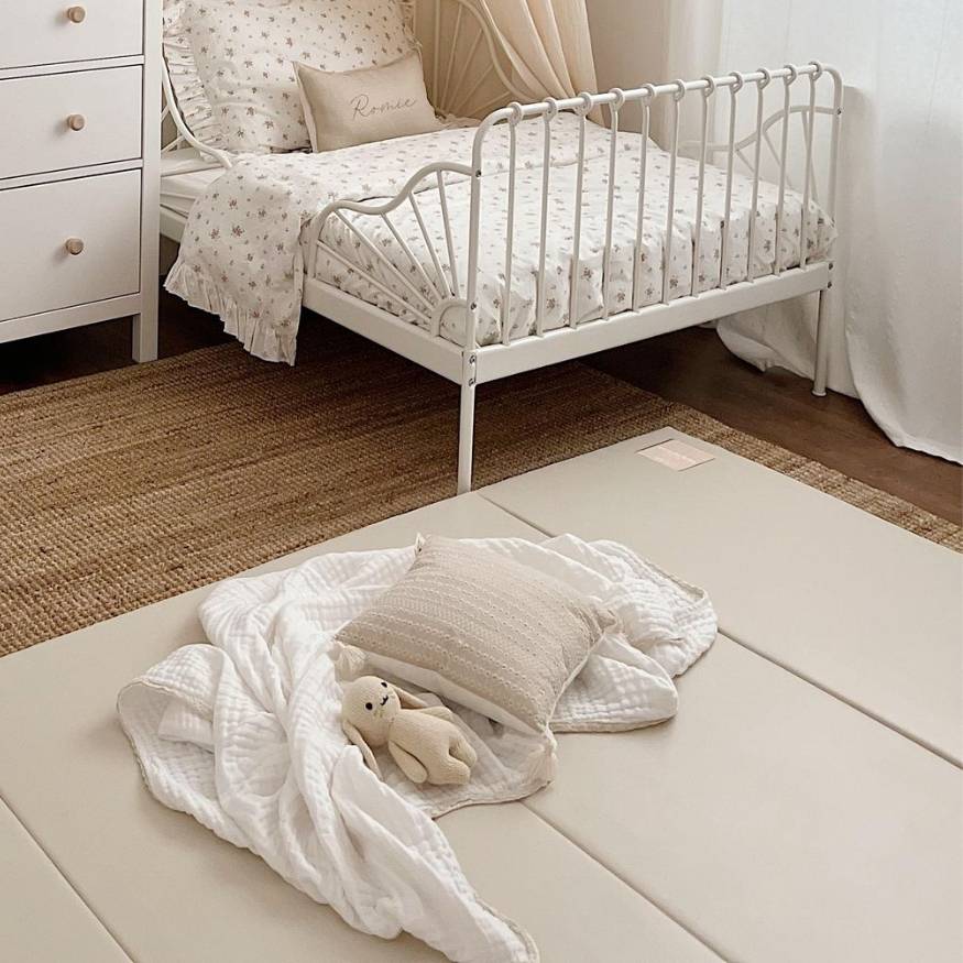 A child's bedroom with a white metal bed and a padded play mat with a stuffed bunny.