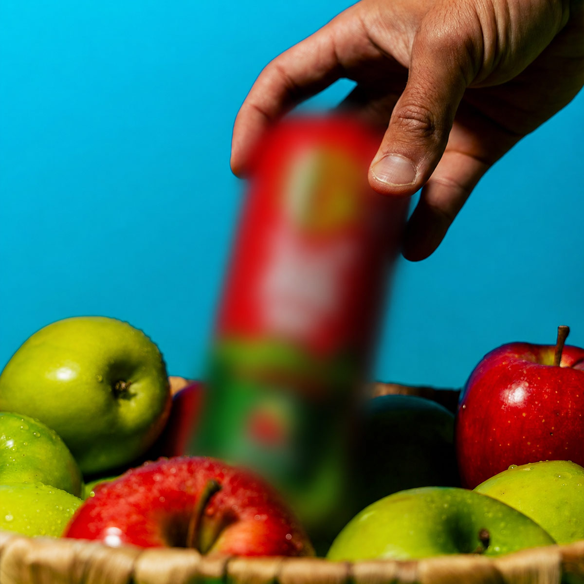A hand picks a can of Gorilla Mind Candy Apple energy drink from a basket of fresh apples.