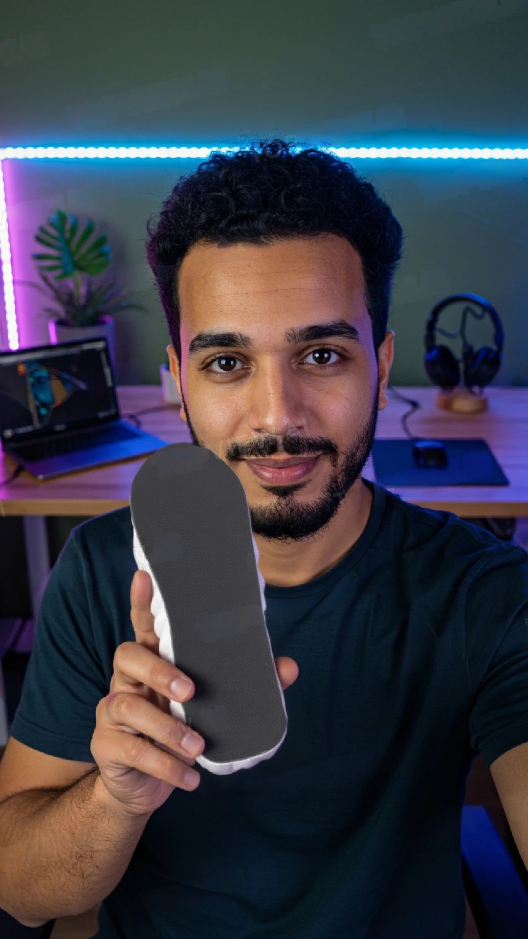 Person holding a shoe insole, with a desk and laptop in the background.