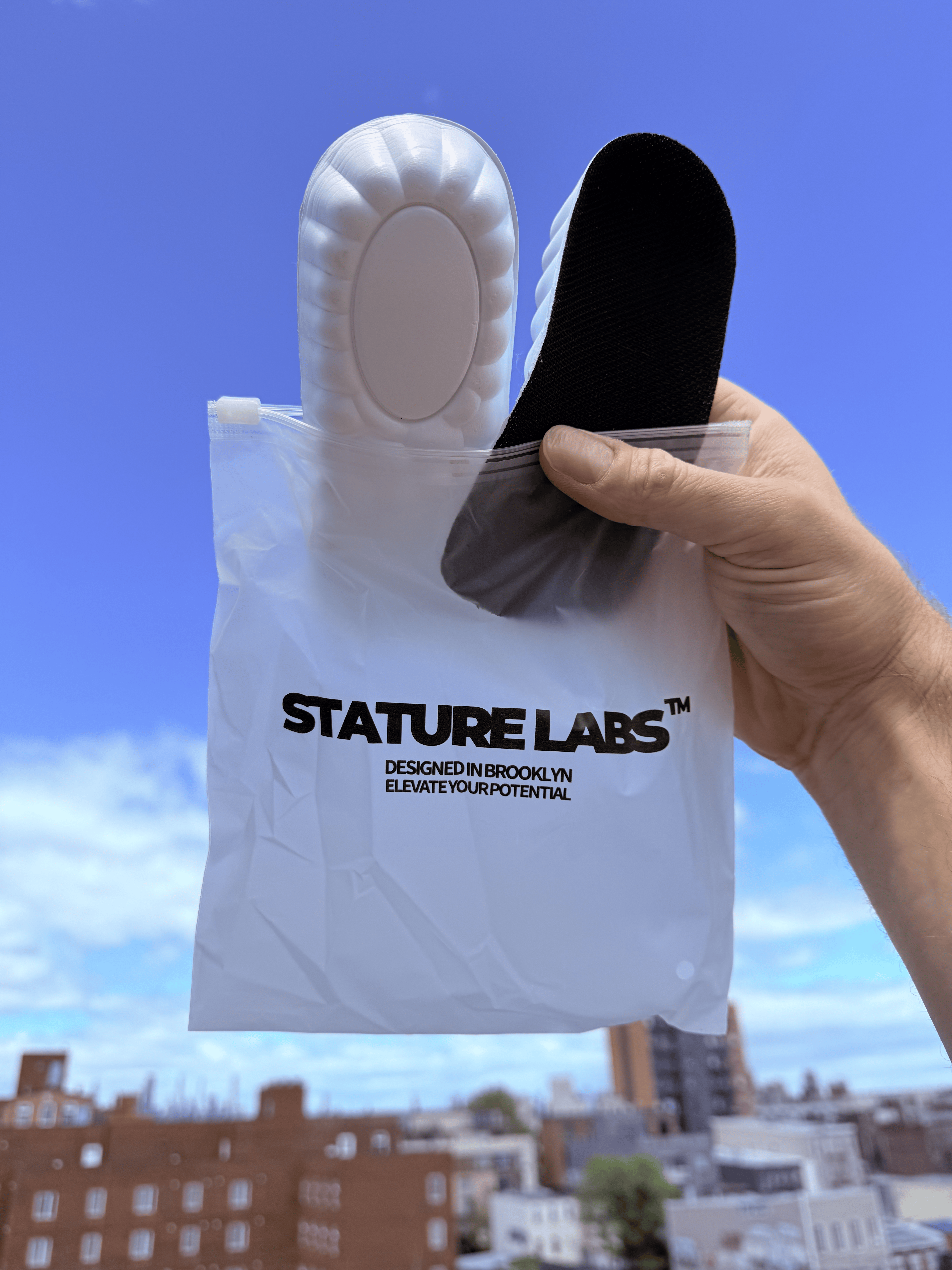 Hand holding Stature Labs insoles against a blue sky background.
