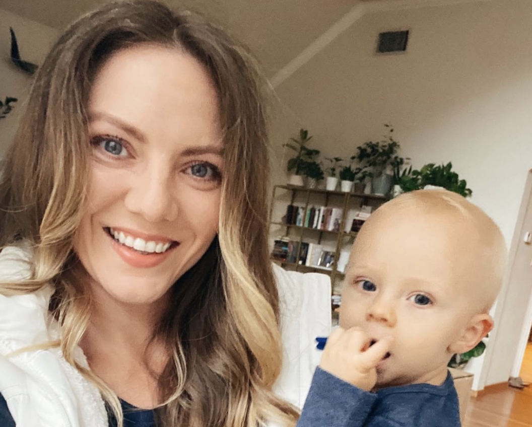 Smiling woman holding a baby in a cozy room with plants.