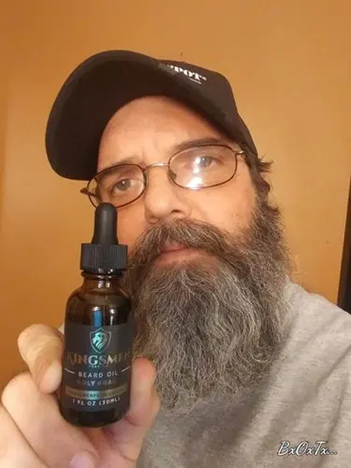 Man with a beard holding a bottle of beard oil.
