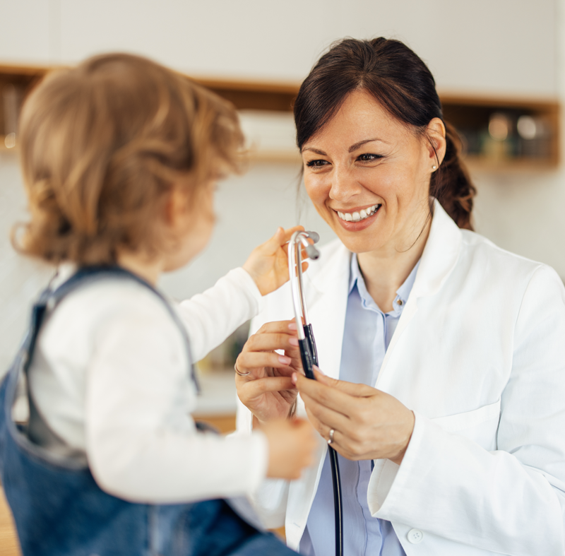 Smiling doctor with stethoscope interacting with a young child.