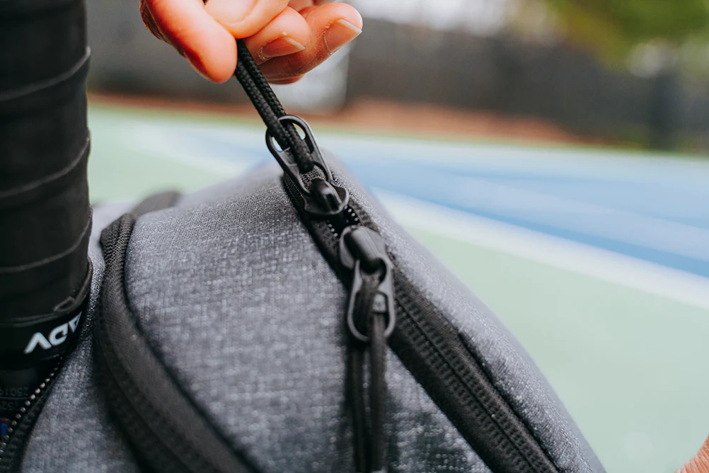 Close-up of a hand holding a zipper on a gray bag.