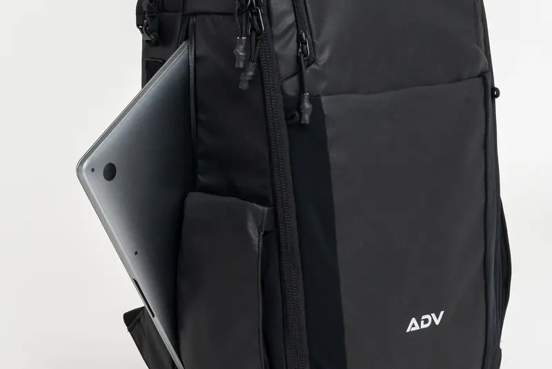 A black backpack with a laptop partially inserted in a side pocket.