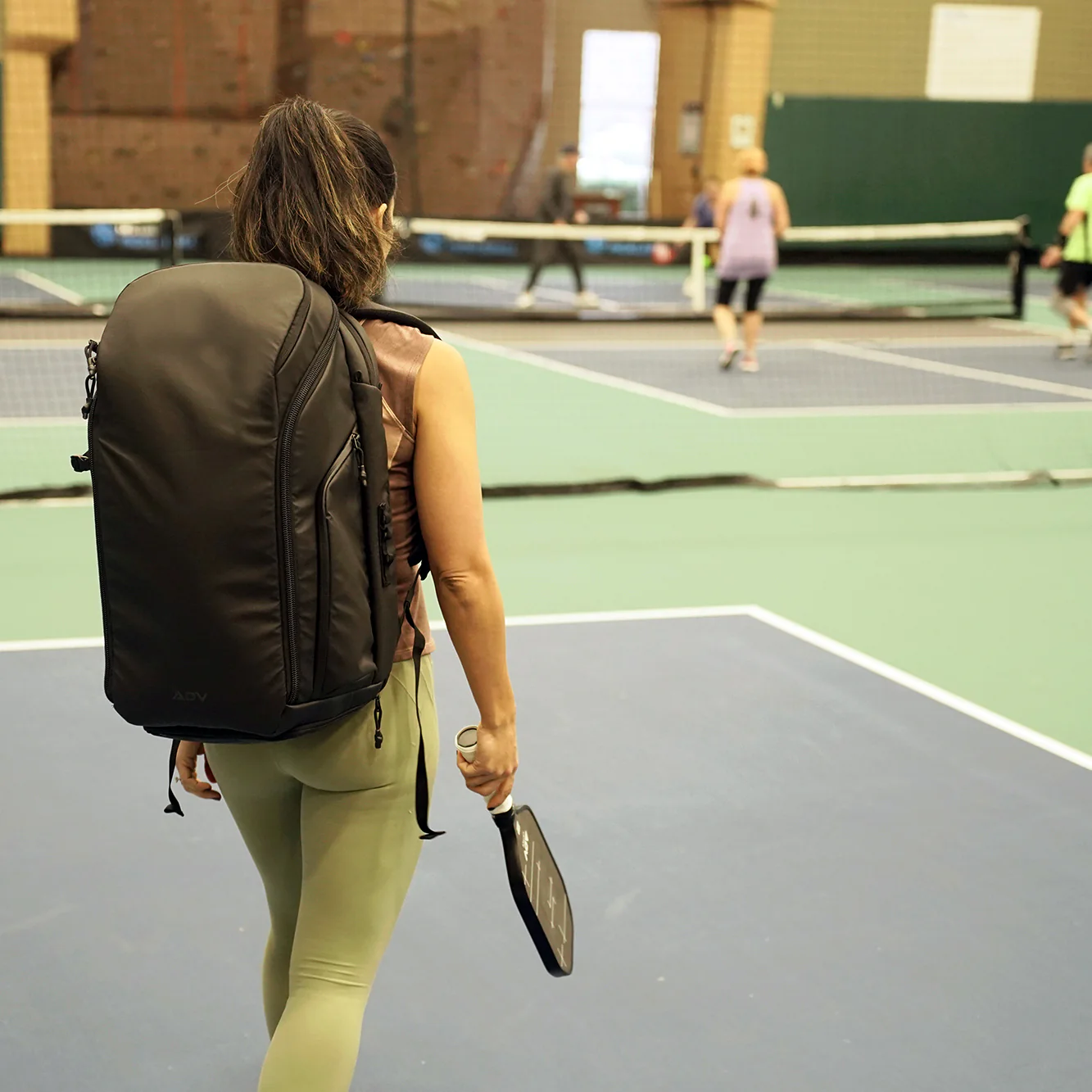 Person with backpack and paddle on indoor tennis court.