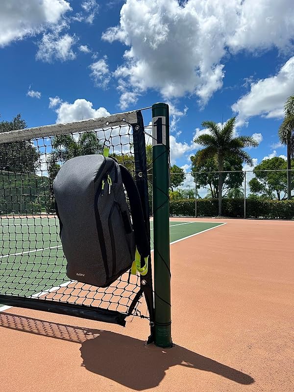 Backpack hanging on a tennis net under a blue sky with clouds.