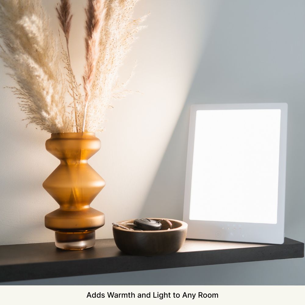 Amber vase with pampas grass, light panel, and wooden bowl on a shelf.