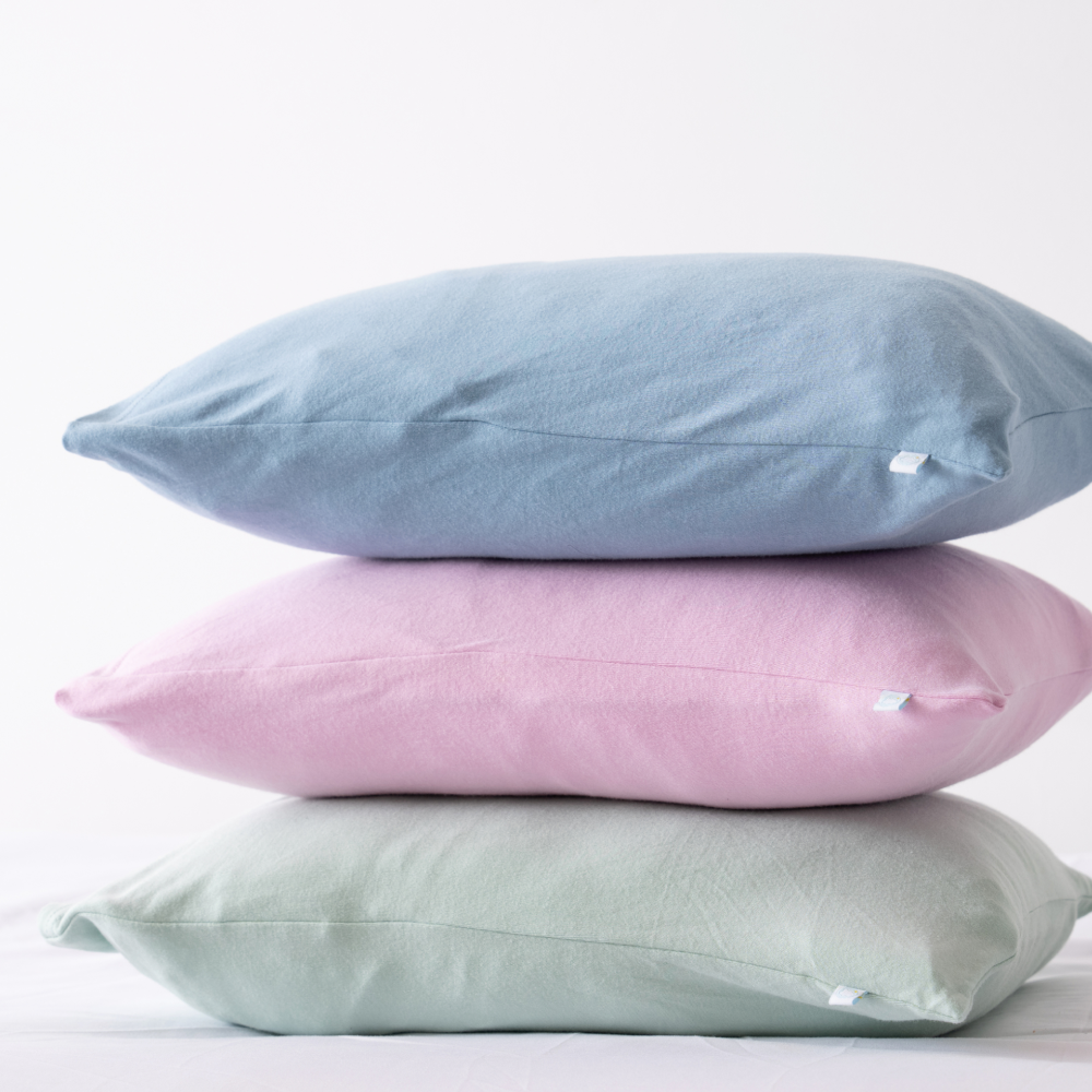 Three stacked pillows in blue, pink, and green on a white background.