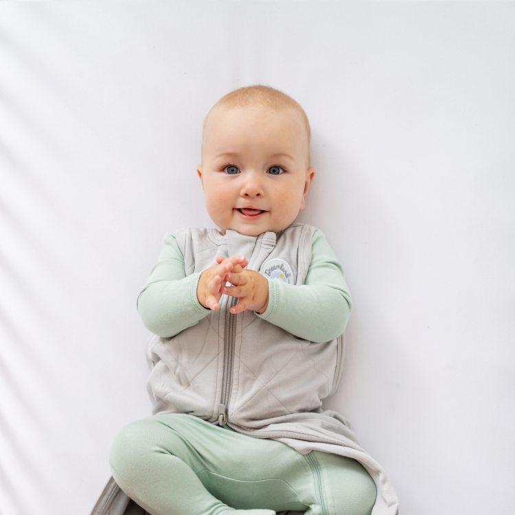 Baby in green outfit sitting on a white surface, smiling.