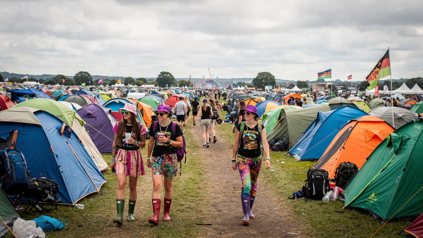 People walk through a large field crowded with colorful tents at an outdoor festival.