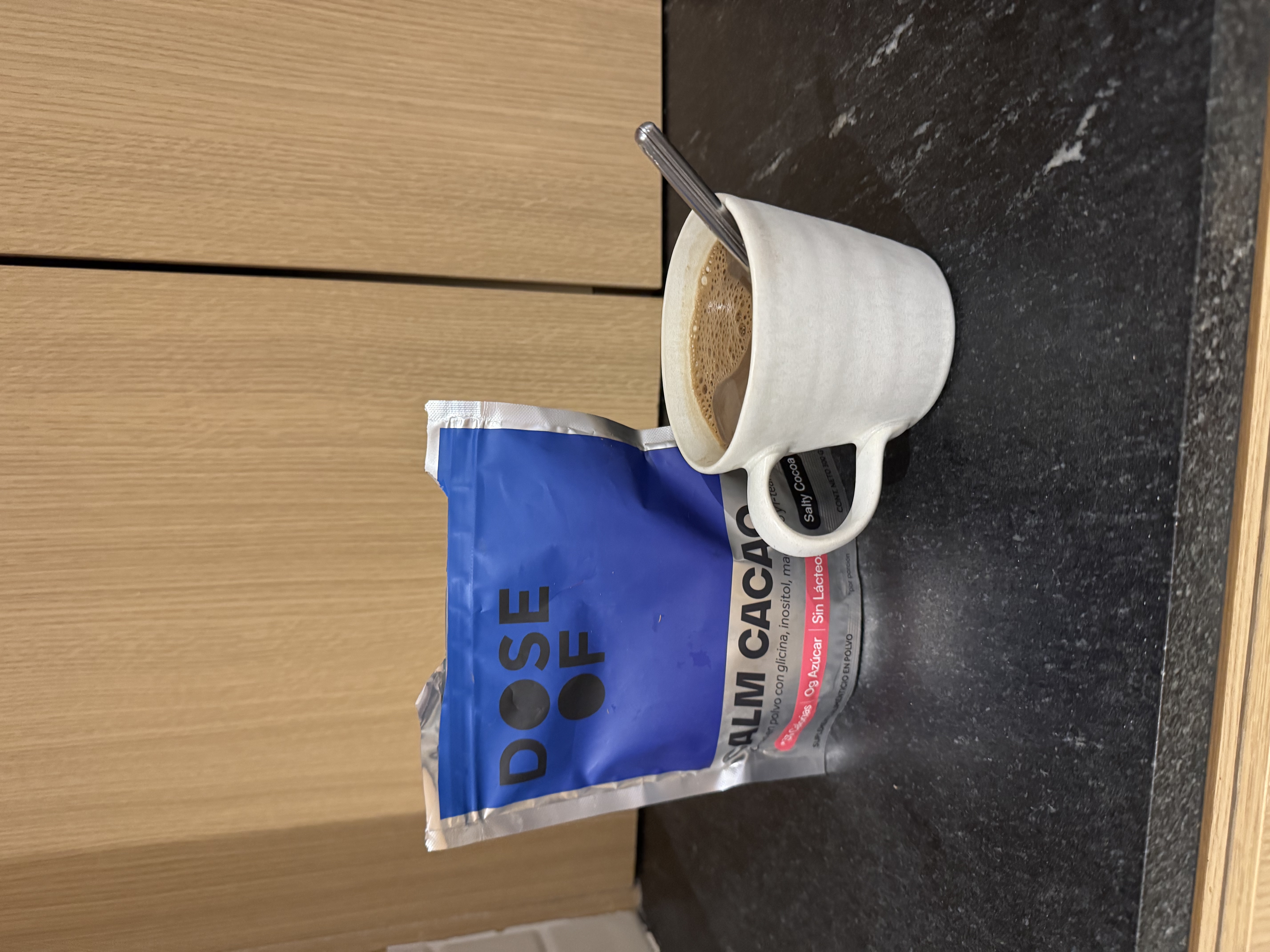 A pack labeled 'Dose of Calm Cacao' next to a white mug with a drink and a spoon.