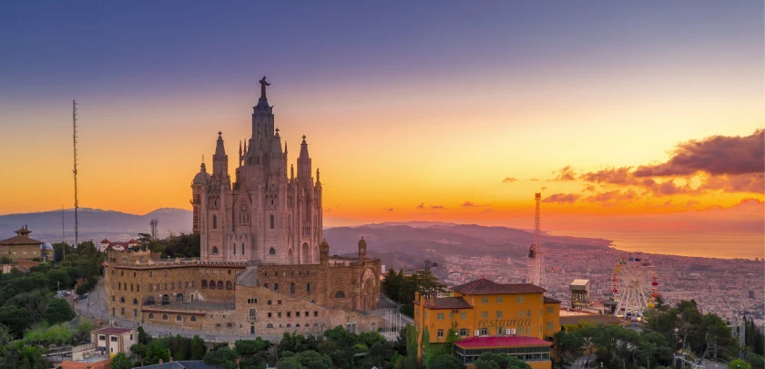 A large cathedral on a hill at sunset with a cityscape in the background.