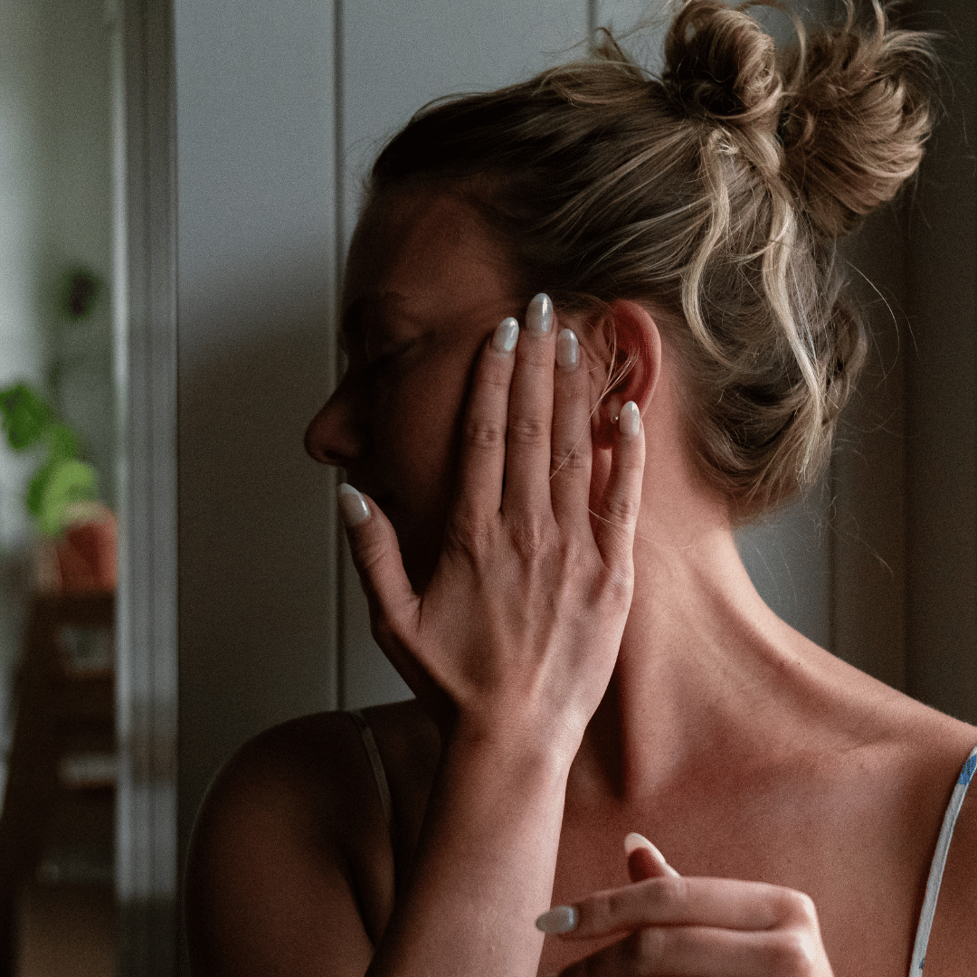 A woman with blonde hair in a messy bun gently touches the side of her face.