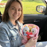 A woman in a car holds a bouquet made of two plush penguins and a red heart.