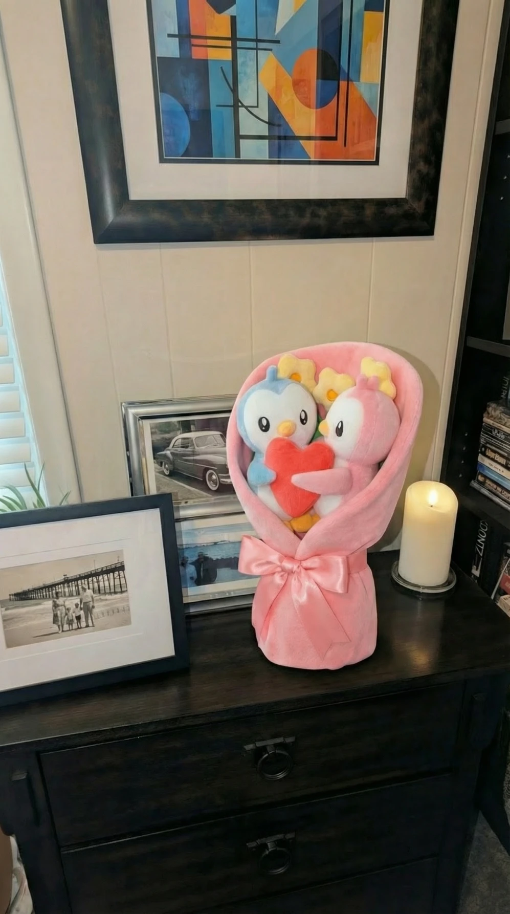 A plush bouquet with a blue and a pink penguin holding a red heart on a dresser.