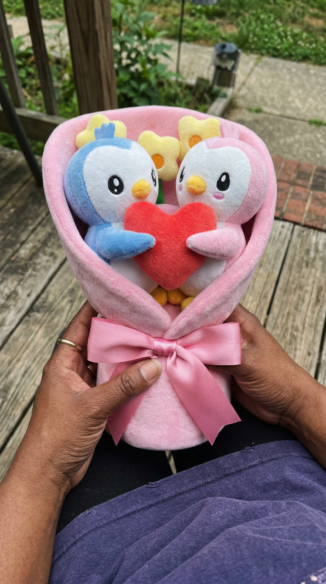 A person holds a plush bouquet of two penguins holding a red heart.