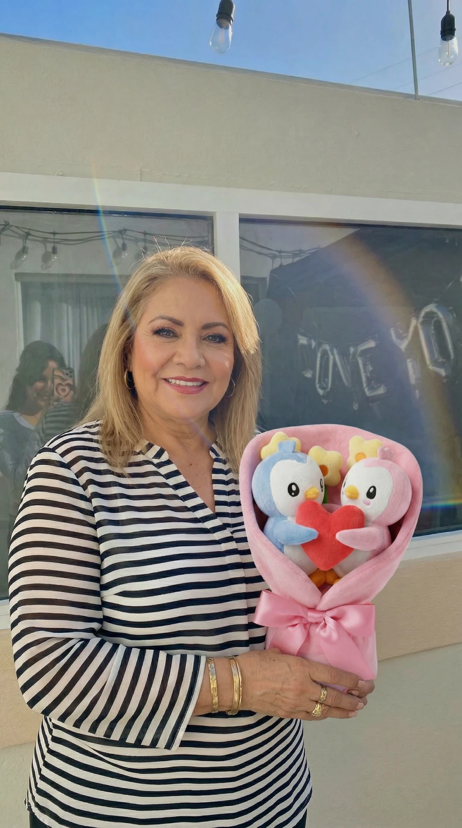A woman in a striped shirt smiles while holding a bouquet of stuffed penguins.