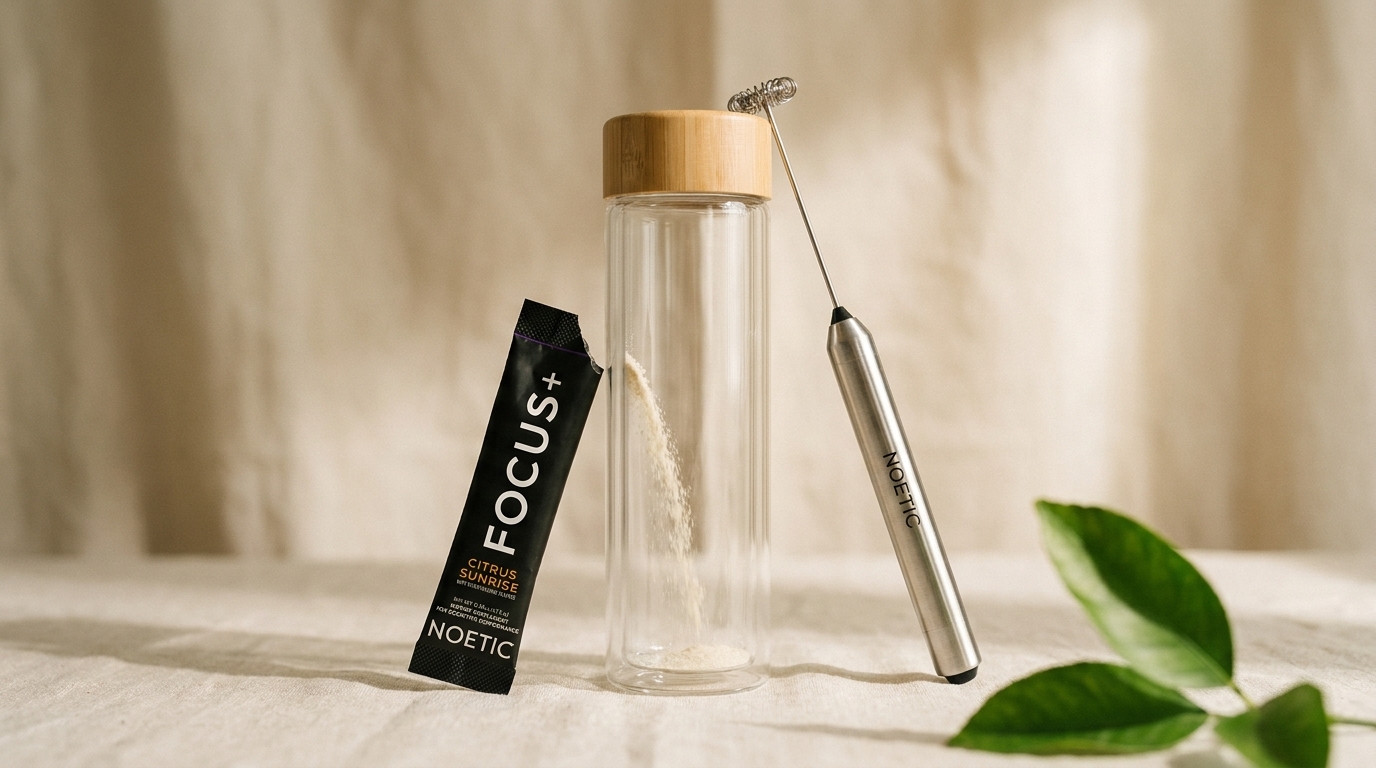 Noetic Focus+ powder is poured from a packet into a glass bottle next to a handheld mixer.