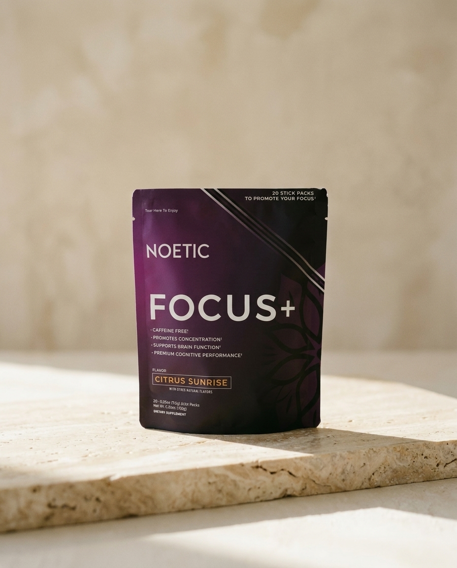 A purple and black pouch of Noetic Focus+ dietary supplement resting on a stone surface.