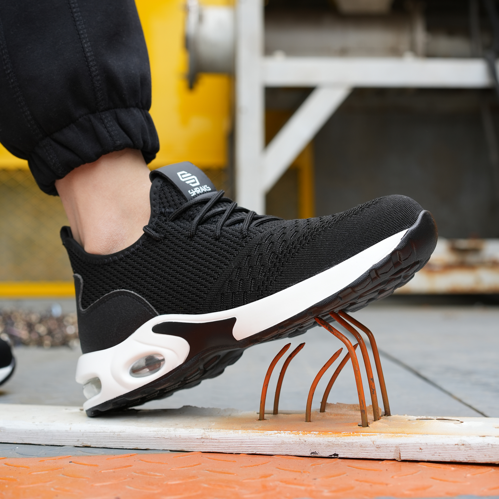 A black safety shoe with a white sole presses down on a bed of rusty nails.