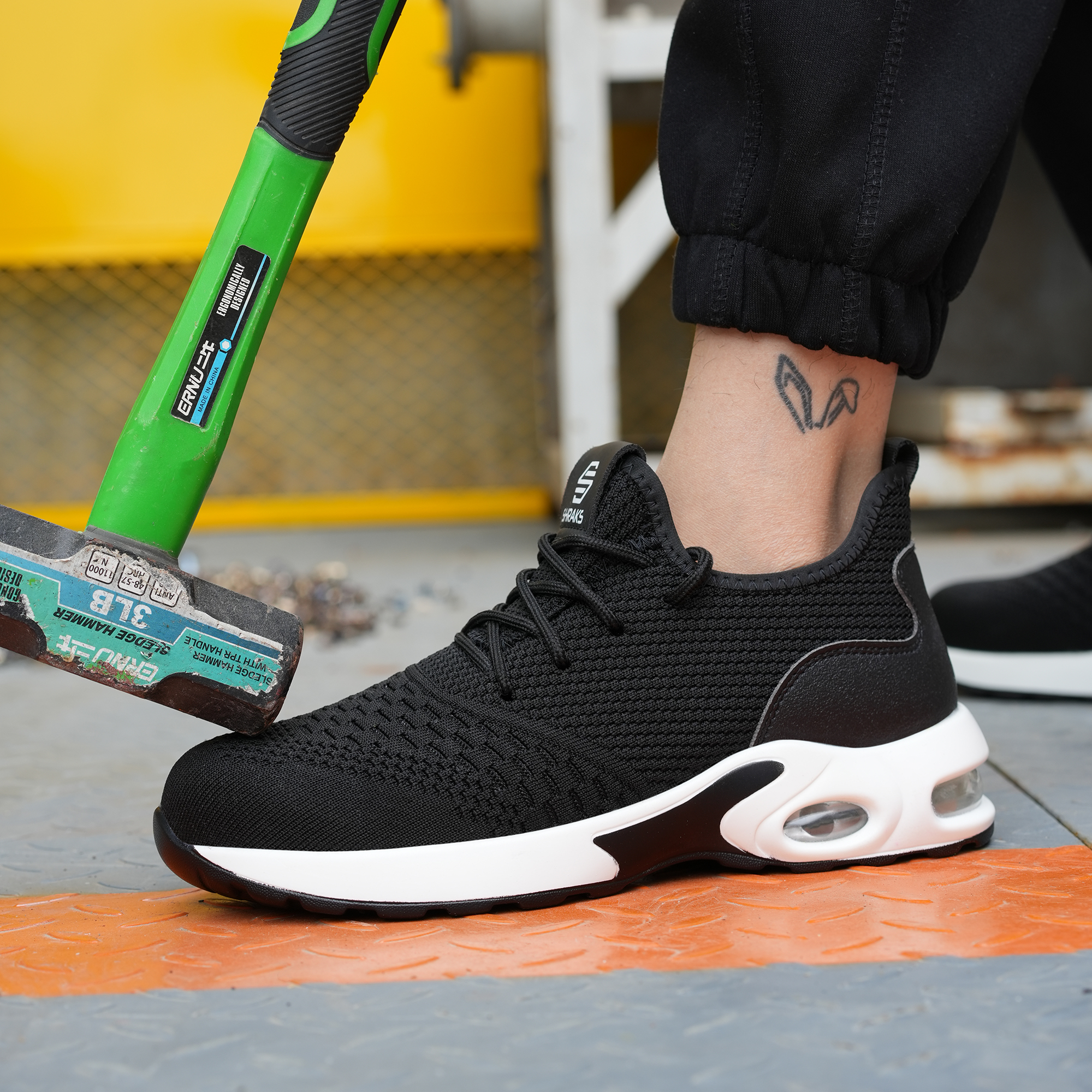 A green sledgehammer rests on the toe of a person's black and white safety shoe.