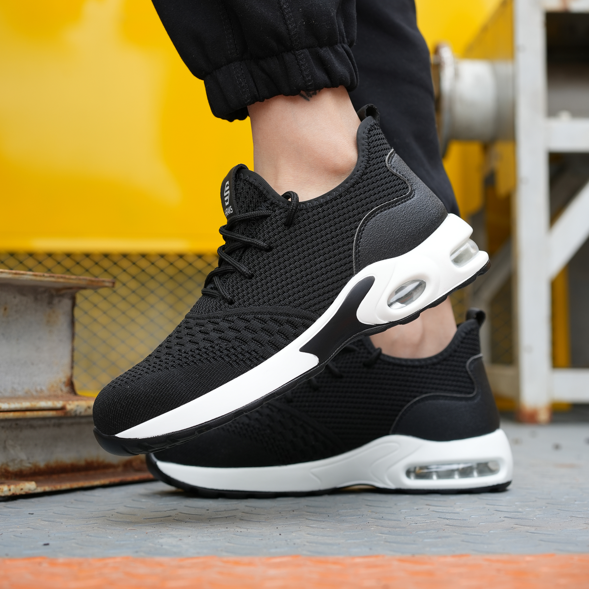 A person's feet wearing black and white sneakers with thick, air-cushioned soles on a metal surface.