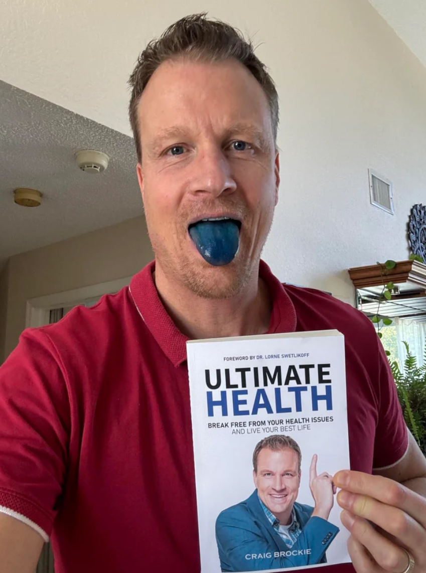 Person with blue tongue holding a book titled 'Ultimate Health.'