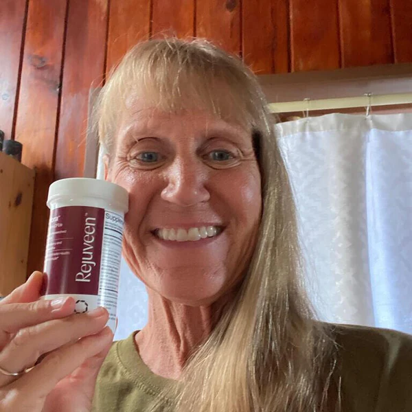 Person smiling and holding a bottle labeled 'Rejuveen' in a wooden room.