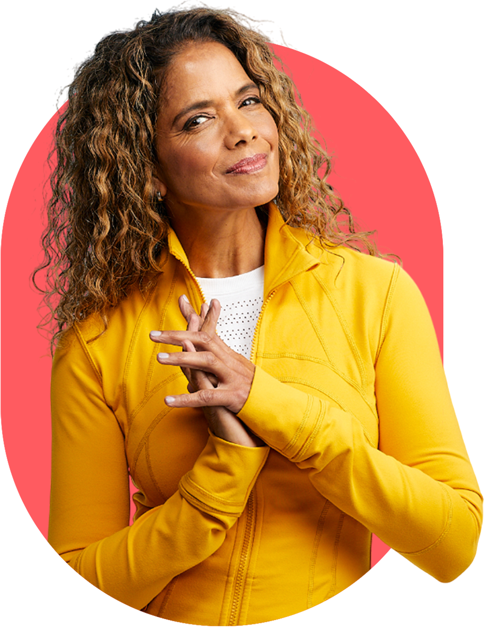Person in a yellow jacket against a red background, smiling with hands clasped.