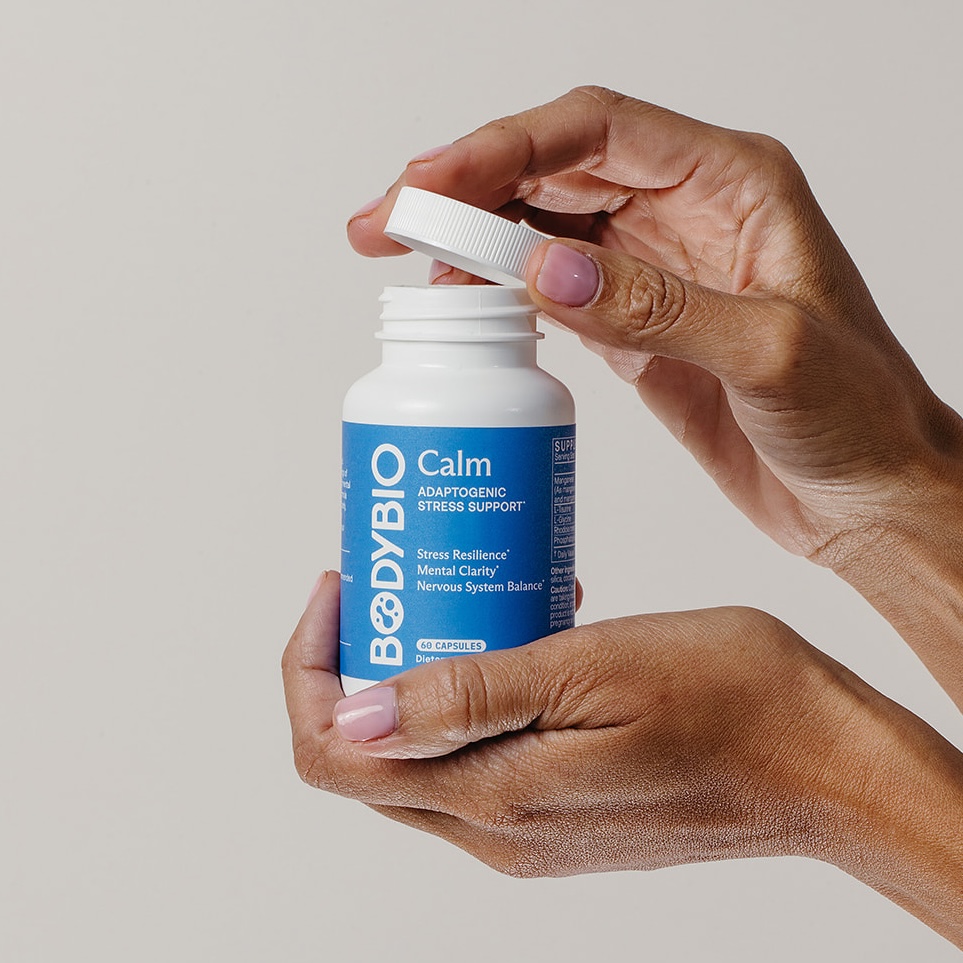 Hands opening a bottle of BodyBio Calm supplement.
