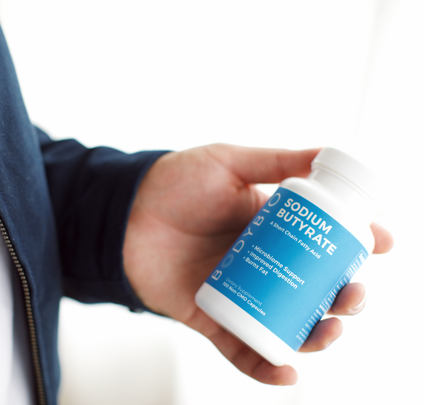 Hand holding a bottle labeled 'Sodium Butyrate' with a blue label.