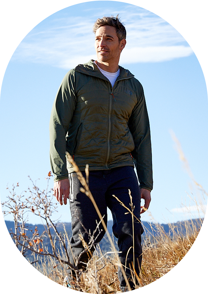 Man in a green jacket walking outdoors on a sunny day.