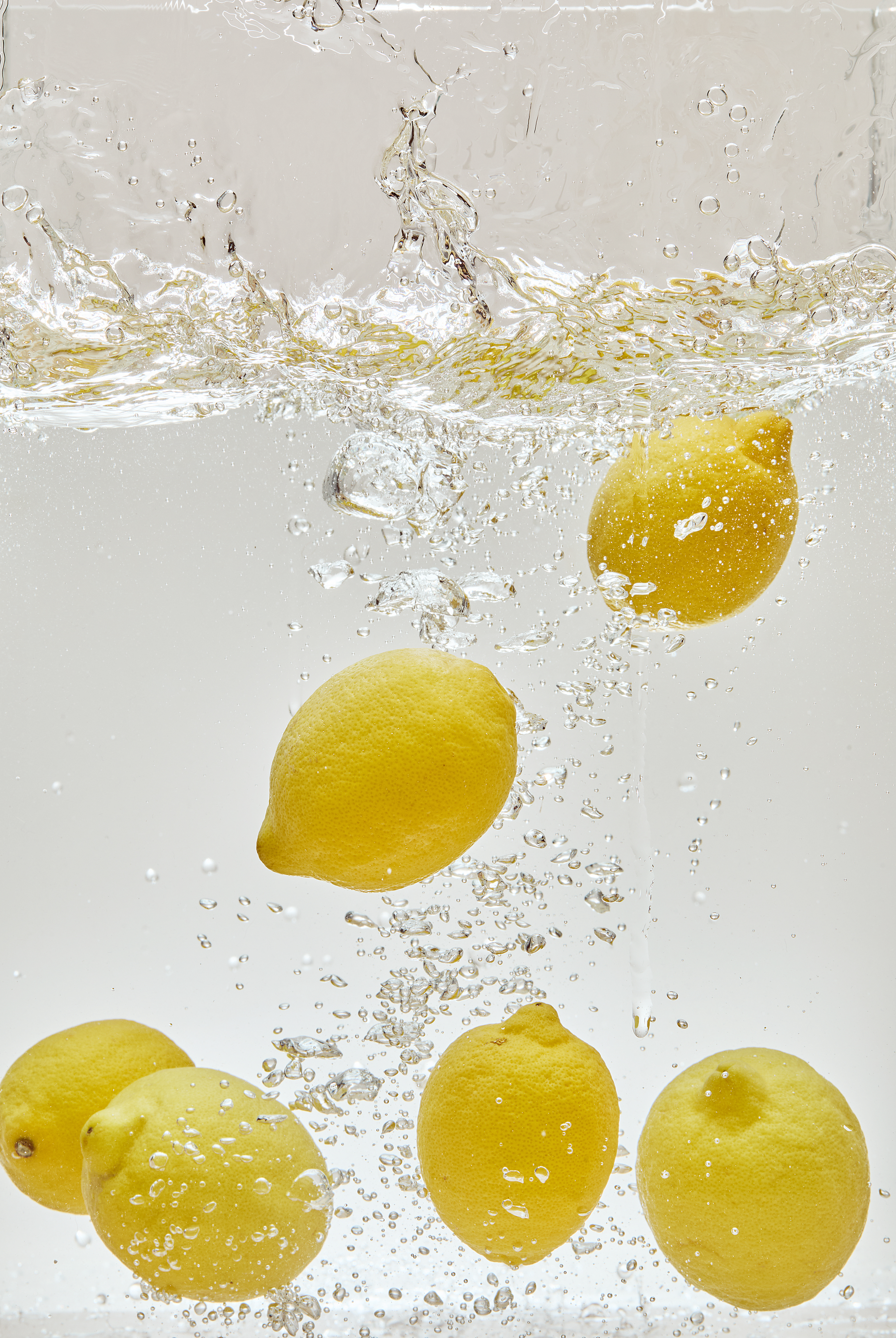 Several whole lemons splashing into clear water, creating bubbles against a white background.