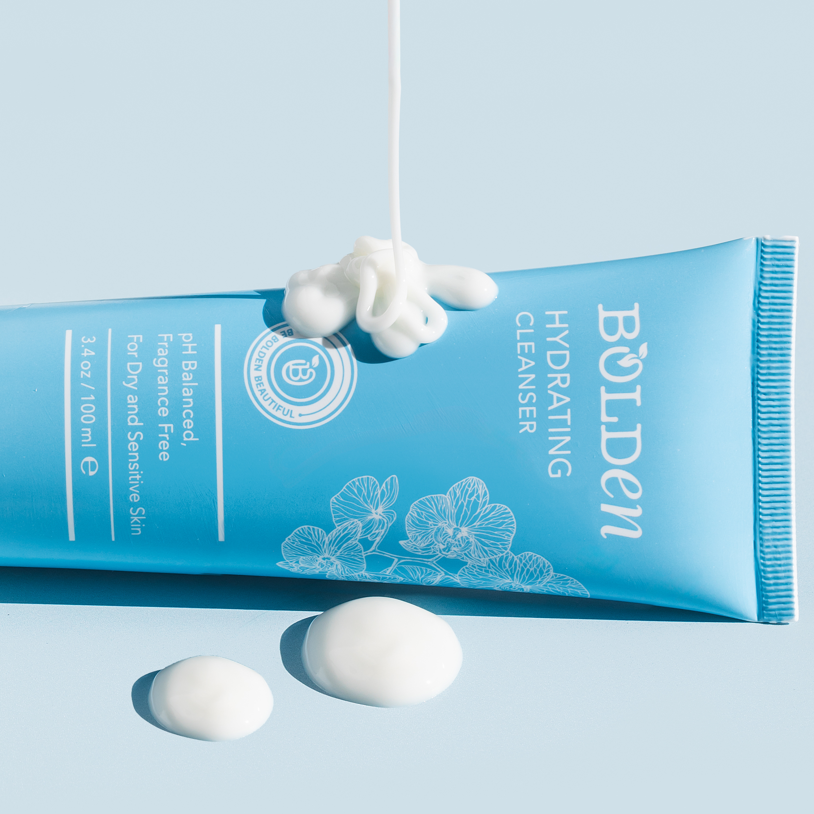 A stream of white lotion is squeezed from a blue tube of Bolden Hydrating Cleanser.